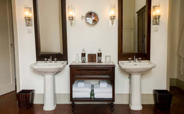 Amangalla suite bathroom with twin pedestal sinks, mirrors, and wooden shelf below.