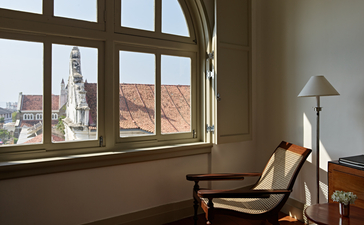 Amangalla suite with large windows framing city views, contemporary chair, and warm natural light.