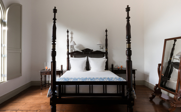 Black four-poster bed in a principal bedroom at Amangalla, with tall finials and white bedding.