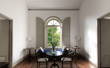 Arched window framing garden views in a suite at Amangalla, with two chairs positioned in the bright, minimalist space.