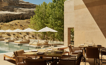 Amangiri restaurant terrace with dining tables, chairs and umbrellas overlooking desert rock formations.