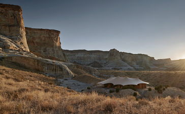 Pavilion exterior at Amangiri resort, with earthen structures set against desert landscape and distant cliffs.