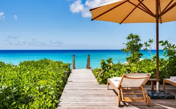 Wooden beach path leading to turquoise waters at Amanyara, with sun umbrella and seating in foreground.