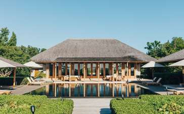安缦涯澜度假村的四卧海滩别墅外观，茅草顶主建筑面向绿地和水景。