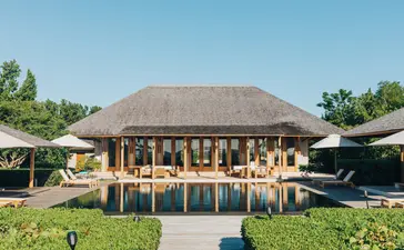Four-bedroom beach sala villa with thatched roof at Amanyara, Turks and Caicos, viewed from manicured gardens.