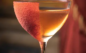 安缦威尼斯酒店的标志性鸡尾酒"Devozione"，杯中盛有琥珀色饮品，饰以红色柑橘片。