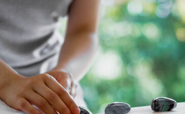 Therapist placing hot stones on a guest's back during a wellness treatment at Amanemu resort.