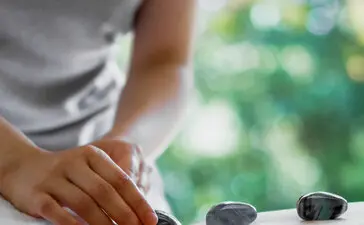 Therapist placing hot stones on a guest's back during a wellness treatment at Amanemu resort.