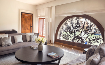 Salon avec canapé gris, table ronde noire et vitrail arqué à Aman Venice.