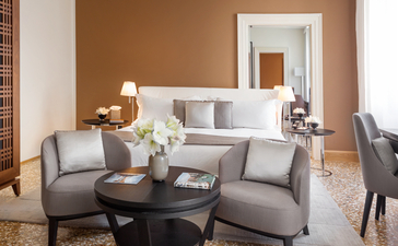 Palazzo chamber luminoso at Aman Venice: serene sitting room with grey upholstered seating, warm terracotta walls, and natural light from tall windows.
