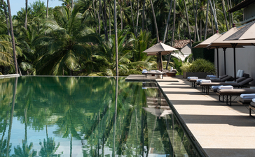 Reflection pool with palm trees at Amanwella, lined by sun loungers and pavilions.