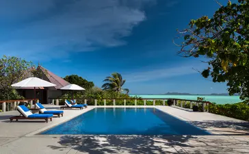Piscina infinita con tumbonas azules y pabellón junto a playa tropical en Amanpulo.