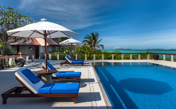 Piscina con lettini blu e ombrelloni bianchi affacciati sul mare, Amanpulo resort.
