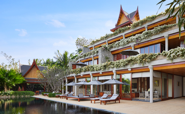 Amanpuri resort's waterfront pavilion with traditional Thai architecture and golden temple-style roofs reflected in calm waters.