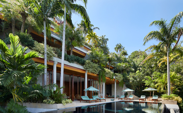 Amanpuri resort in Thailand, modern pavilion with teak wood architecture surrounded by tropical palms and reflecting pool.