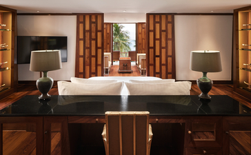 Principal bedroom at Amanpuri with wooden furnishings, white bed, and warm lighting from bedside lamps.