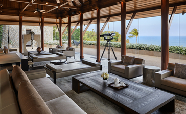 Amanpuri ocean villa lounge with wooden beams, ocean views, and contemporary furnishings overlooking the coastline.