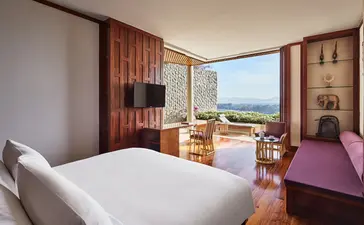 Principal bedroom with ocean views at Amanpuri, featuring warm wood furnishings and a balcony overlooking the coast.