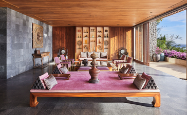 アマンプリのリゾートのラウンジ。紫のラグの上に木製家具が配置され、大きな窓から海の景色が見える。