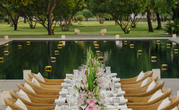 Long table set for celebration at Amantaka, with wooden chairs and floral arrangements beside a reflecting pool.