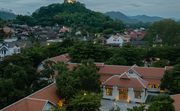 Amantaka residence with terracotta roof overlooking misty mountains and valley town at dusk.