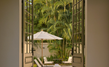 Khan Pool Suite outdoor terrace at Amantaka, looking through open doors to poolside seating and lush gardens.