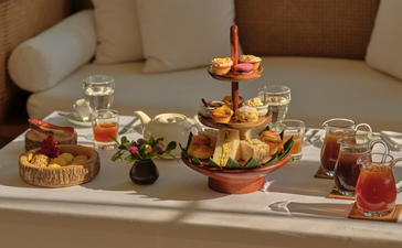 Afternoon tea service at Amantaka, featuring tiered cake stand with pastries, teapot, and assorted cups on white table.