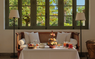 Afternoon tea service laid out on a table in the library at Amantaka, with large windows overlooking verdant gardens.