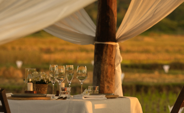 Intimate outdoor dining table set at Amantaka with draped fabric canopy and countryside views at dusk.