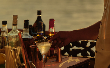 Cocktail-making session during a Mekong sunset cruise at Amantaka, with spirit bottles and mixing tools arranged on a wooden table.