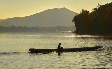 Local fisherman in traditional wooden boat on the Mekong River at sunset, Amantaka.