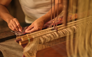 Hands working on traditional Laotian silk textile weaving at Amantaka.