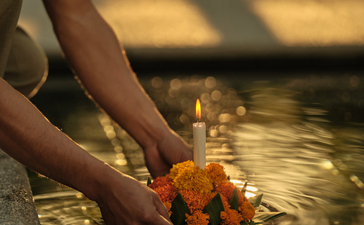 Hands releasing a lit flower krathong into water during Loy Krathong ceremony at Amantaka.