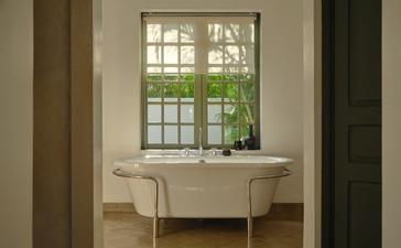 Freestanding bathtub positioned beneath a latticed window at Amantaka, framed by neutral walls and natural light.