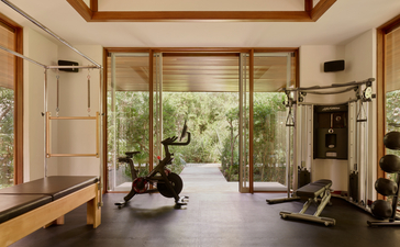 Amanyara gym with floor-to-ceiling glass doors opening onto tropical gardens, featuring exercise equipment and wooden ceiling details.