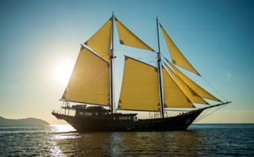 Traditional sailing vessel with golden sails at Amandira, Indonesia, at dusk.