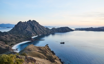 Rugged peaks frame a turquoise bay at Amandira, Indonesia, with a lone boat anchored in calm waters below.