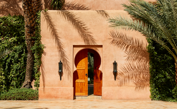 摩洛哥安缦珍纳度假村的建筑细节，土黄色墙面、金色木门和棕榈树环绕的水池。