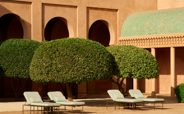 安缦珍纳度假村主泳池，摩洛哥传统建筑与翠绿植被环绕，阳光洒落池面。