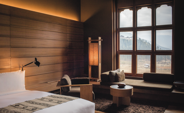 Gangtey Lodge suite bedroom with wooden wall panelling, bed, desk chair and Phobjika Valley view at Amankora, Bhutan.