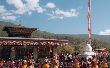 Colourful festival gathering at Amankora in Bumthang, with crowds seated on ground beneath clear blue sky.