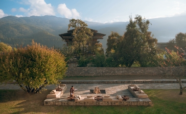 Firepit seating area at Amankora's Bumthang Lodge, overlooking a river valley with forested mountains beyond.