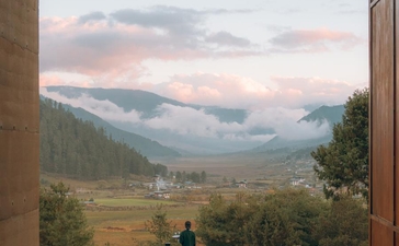 Outdoor dining terrace at Amankora's Gangtey Lodge overlooking a misty valley and forested mountains at dusk.
