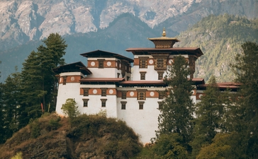 Amankora perched on a cliff in Paro valley, Bhutan, with forested mountains rising behind.