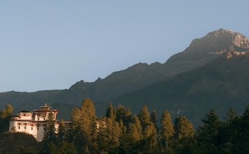 Amankora retreat nestled in a forested valley beneath Paro's mountain peaks at dusk.