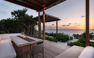 Pavillon de plage d'Amanyara au coucher du soleil, avec terrasse en pierre, mobilier en bois et vue sur l'océan des Turques-et-Caïques.