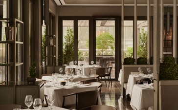 Dining room at Aman New York with round table, large windows overlooking city, and elegant place settings.