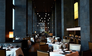 Arva dining room at Aman Tokyo with soaring columns, warm lighting, and diners seated throughout the space.