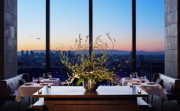 Dining tables set by floor-to-ceiling windows overlooking Tokyo's skyline at sunset, Aman Tokyo.