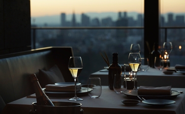 Table setting at Aman Tokyo with Tokyo skyline visible through floor-to-ceiling windows at dusk.